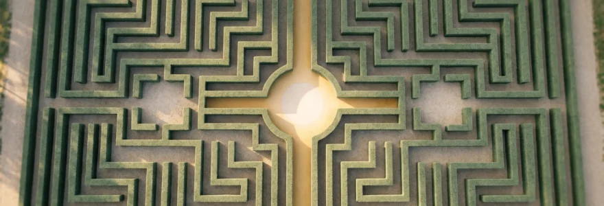 Vue aérienne d'un labyrinthe végétal géométrique avec un chemin doré central menant directement au centre illuminé